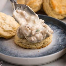 spoon adding sausage gravy to biscuit