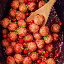 overhead shot of cranberry mustard meatballs in a crock pot with a wooden spoon