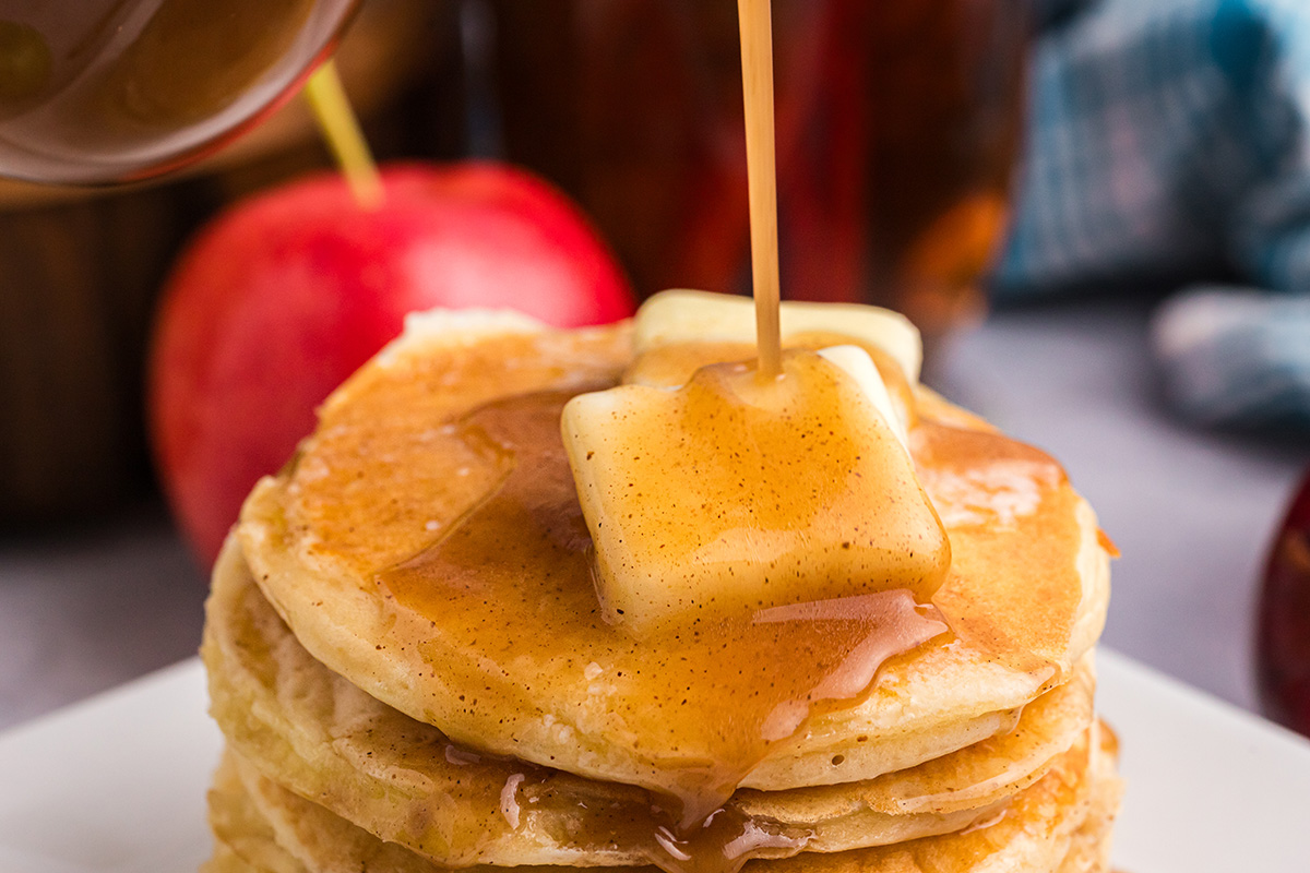 close up shot of syrup poured onto stack of pancakes