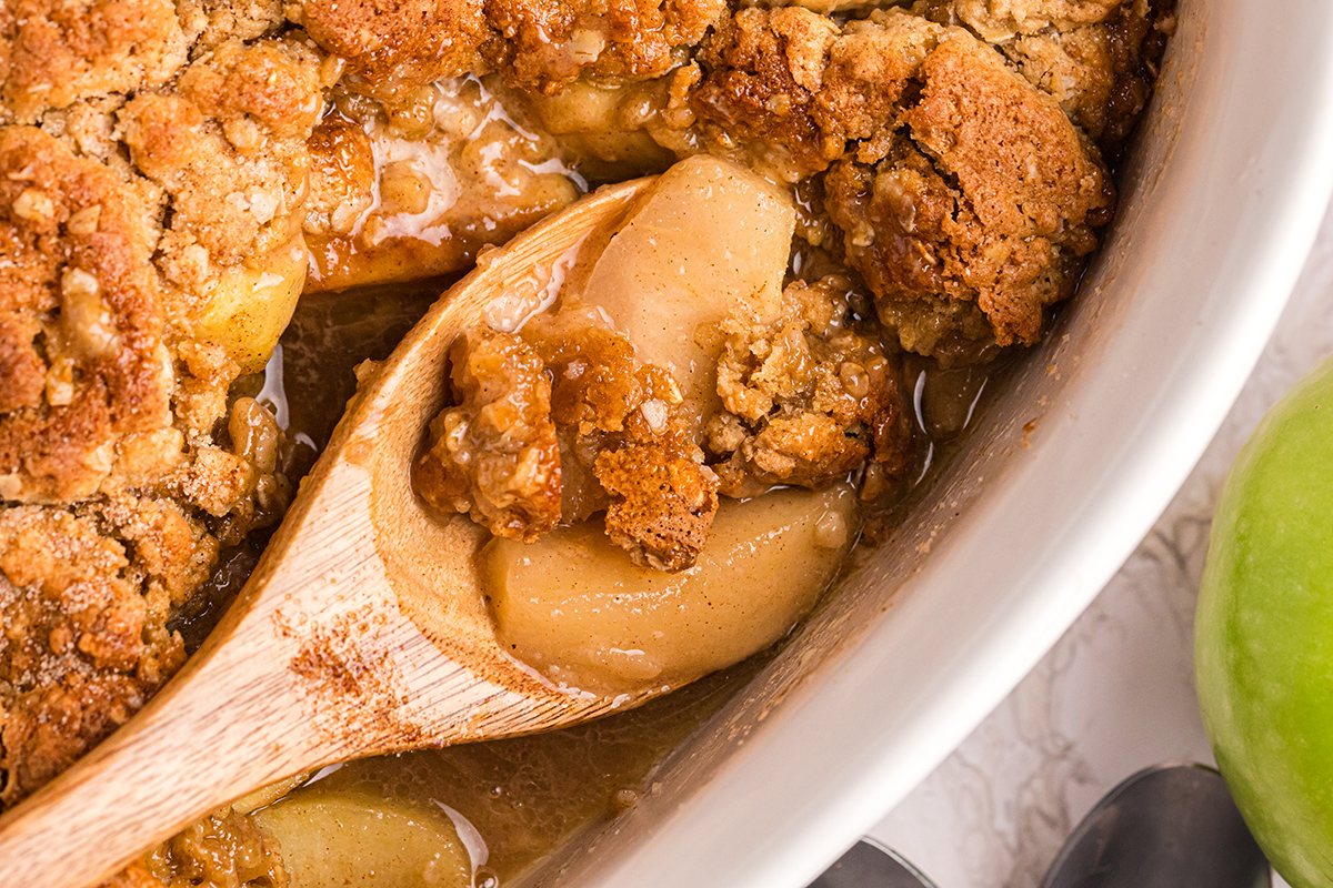 close up overhead shot of wooden spoon in baking dish of apple crisp