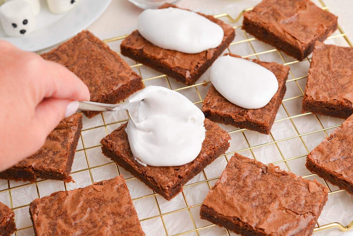 hand spooning marshmallow fluff onto brownies