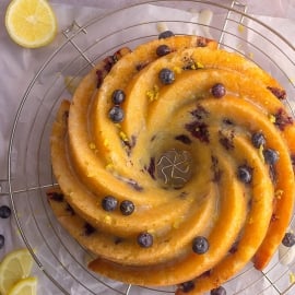 overhead of lemon blueberry cake on a wire cooling rack with fresh blueberries and lemon zest