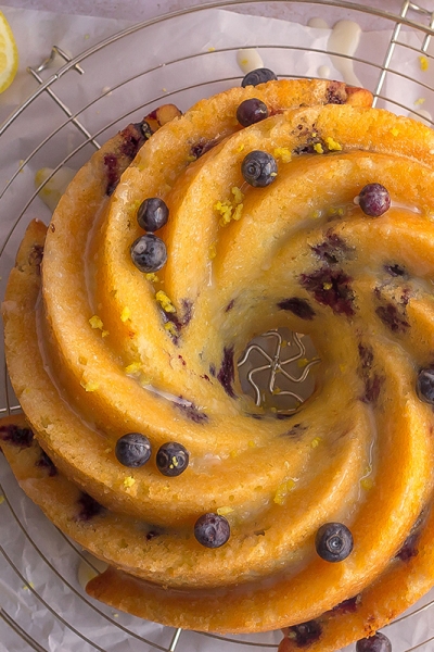 overhead of lemon blueberry cake on a wire cooling rack with fresh blueberries and lemon zest