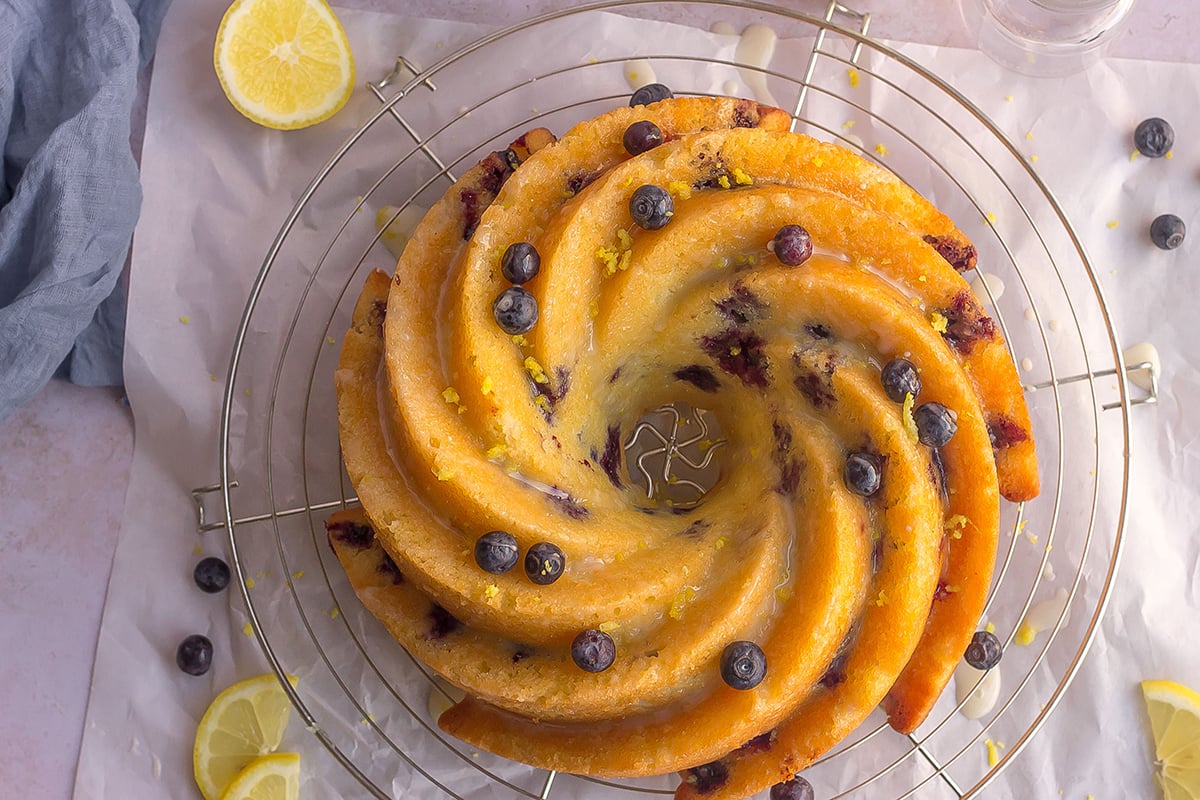 overhead of lemon blueberry cake on a wire cooling rack with fresh blueberries and lemon zest