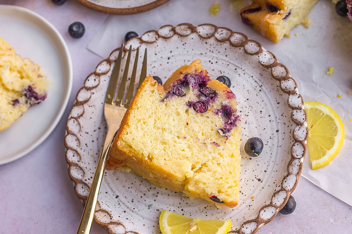 slice of lemon blueberry cake on a white matte serving dish with a fork