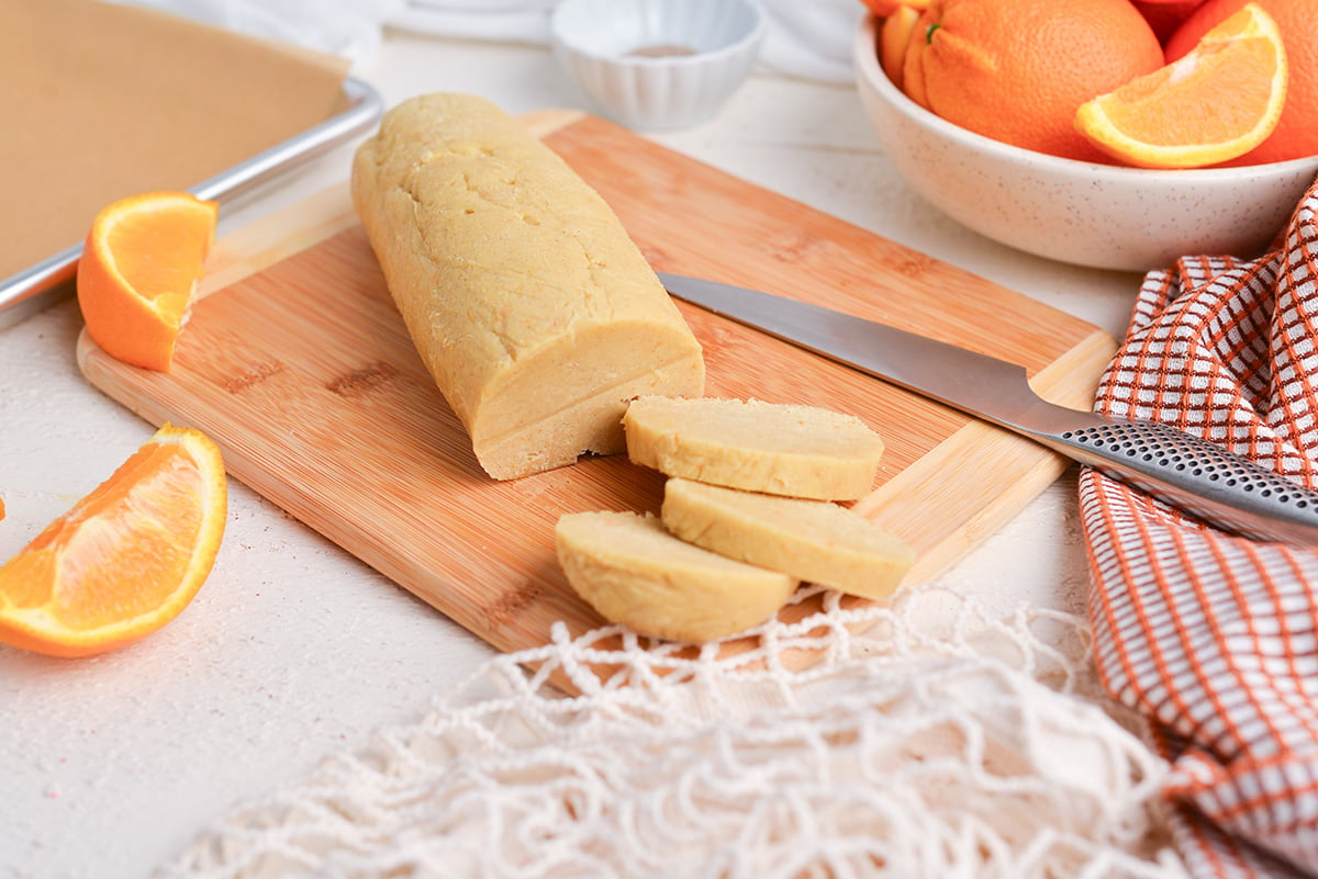 slice and bake cookie dough on a wooden cutting board with fresh oranges