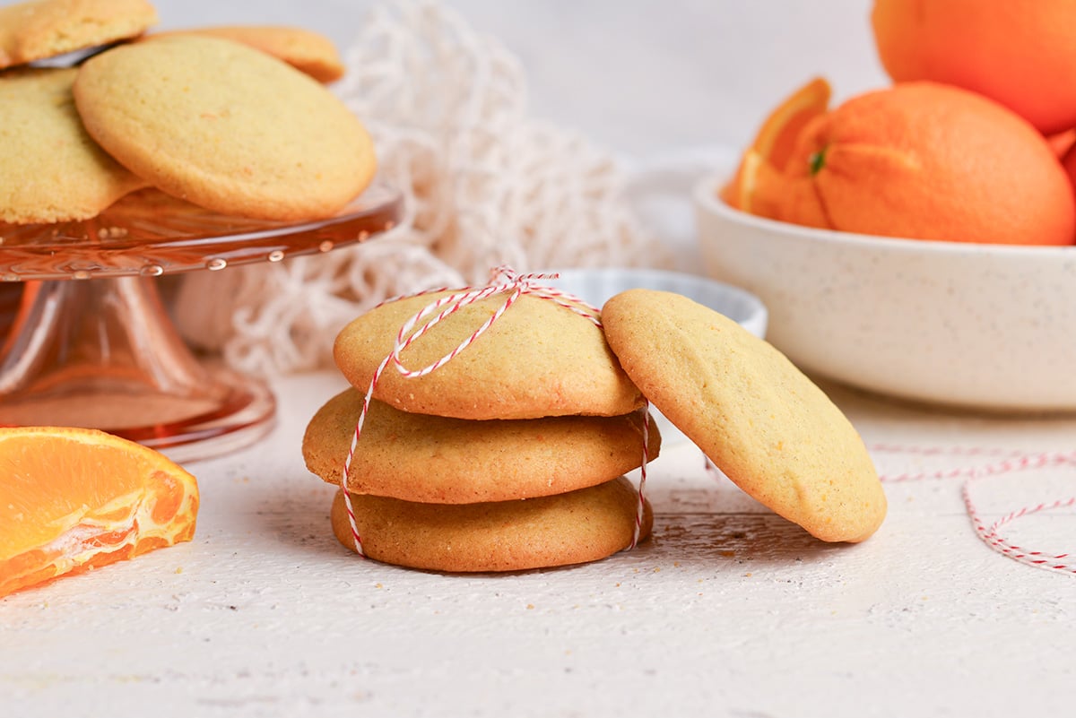 stack of cardamom cookies tied with a red and white string with oranges in the background