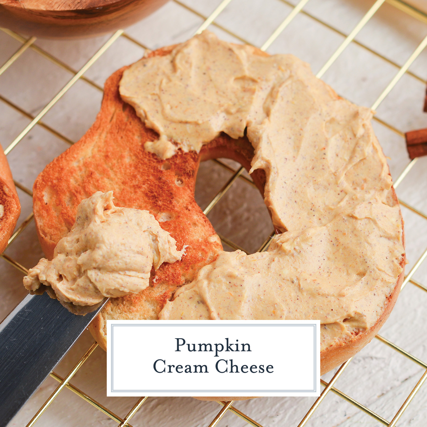 close up angled shot of pumpkin cream cheese spread onto bagel with text overlay for facebook