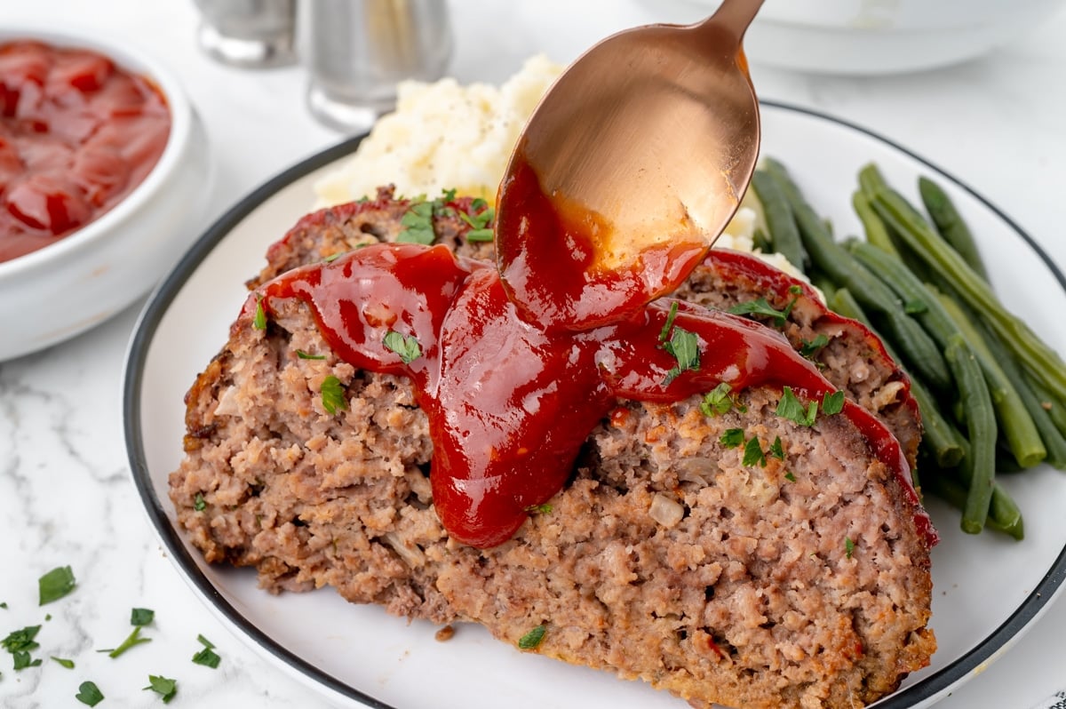 spoon adding sauce to meatloaf slices