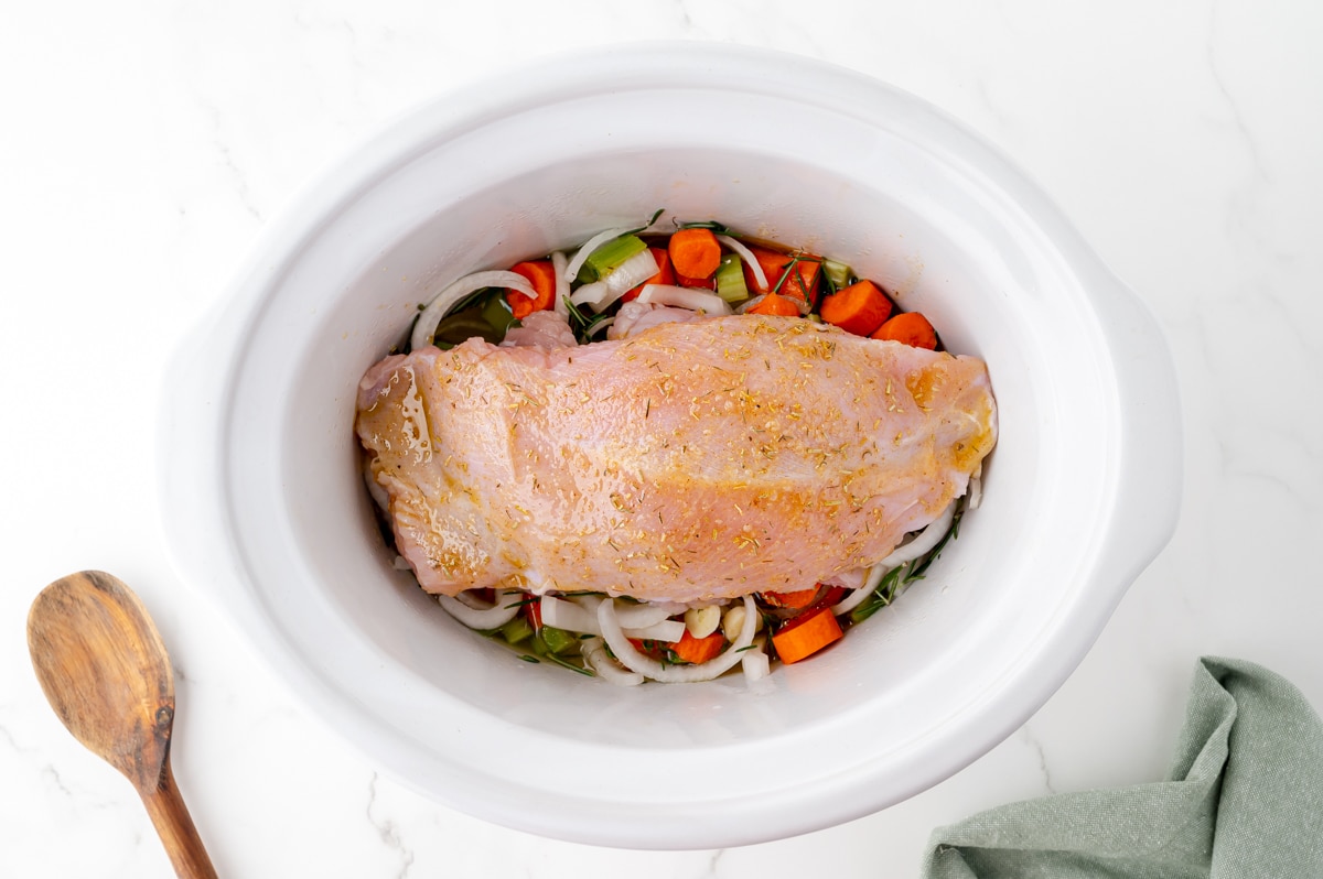 raw turkey breast with seasonings over veggies in slow cooker