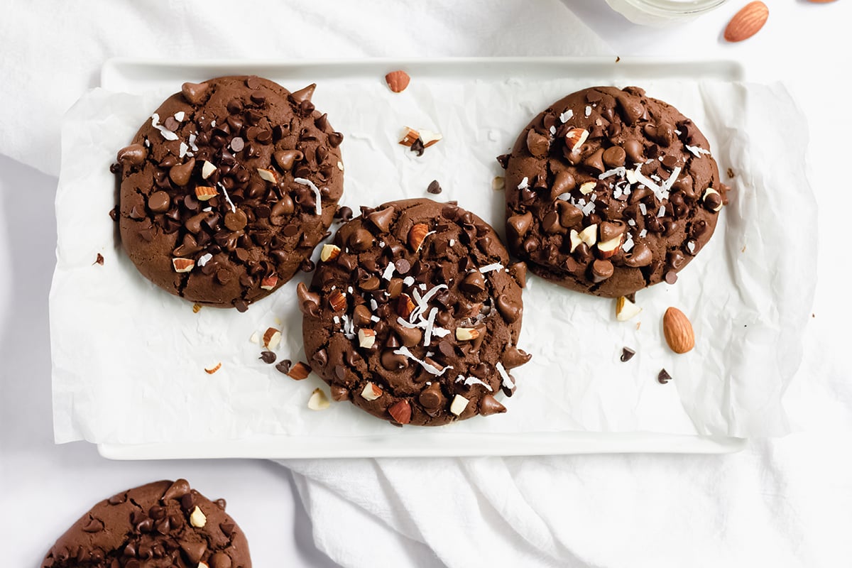 three chocolate cookies with almonds, chocolate chips and shredded coconut on a serving plate