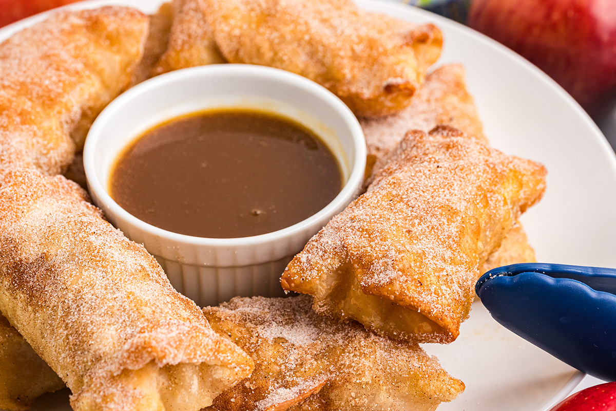 angled shot of platter of dessert egg rolls with bowl of caramel sauce