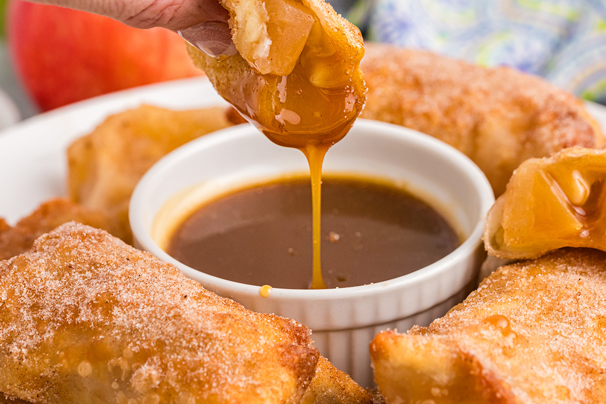 hand dipping apple pie egg roll into caramel sauce