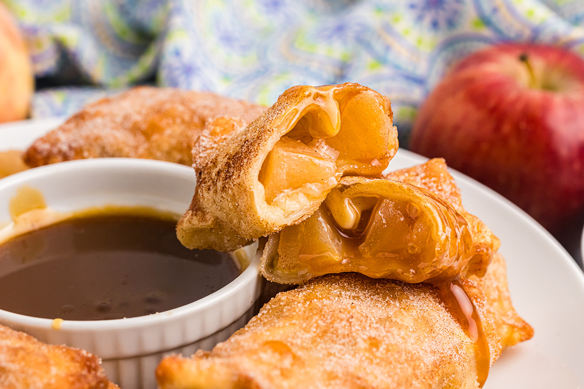 close up of apple pie egg rolls cut in half with bowl of caramel sauce