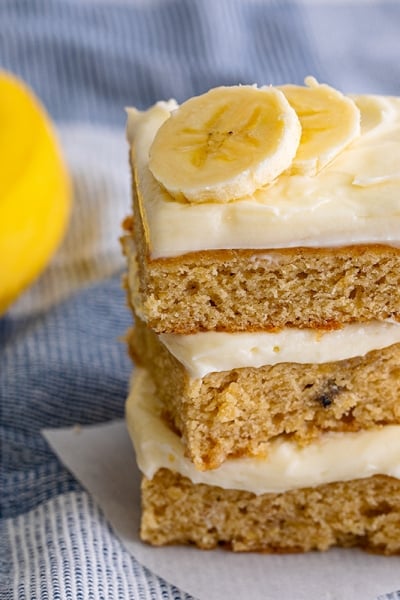 stack of frosted banana blondies with fresh banana slices on top