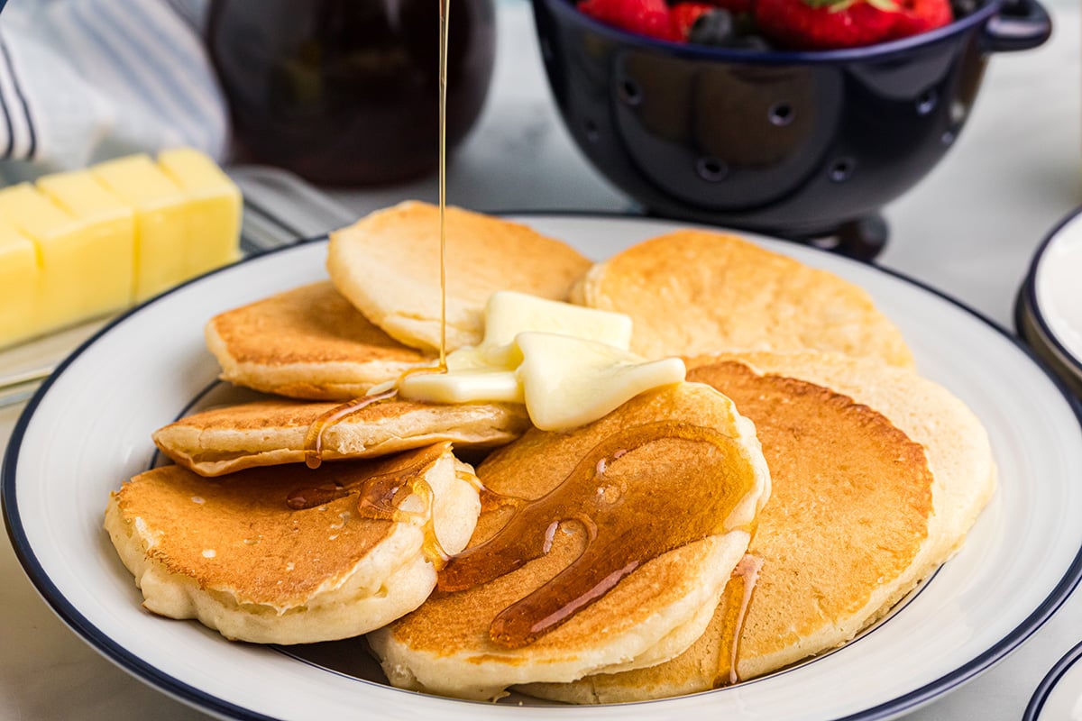 angled shot of syrup poured onto plate of buttermilk pancakes