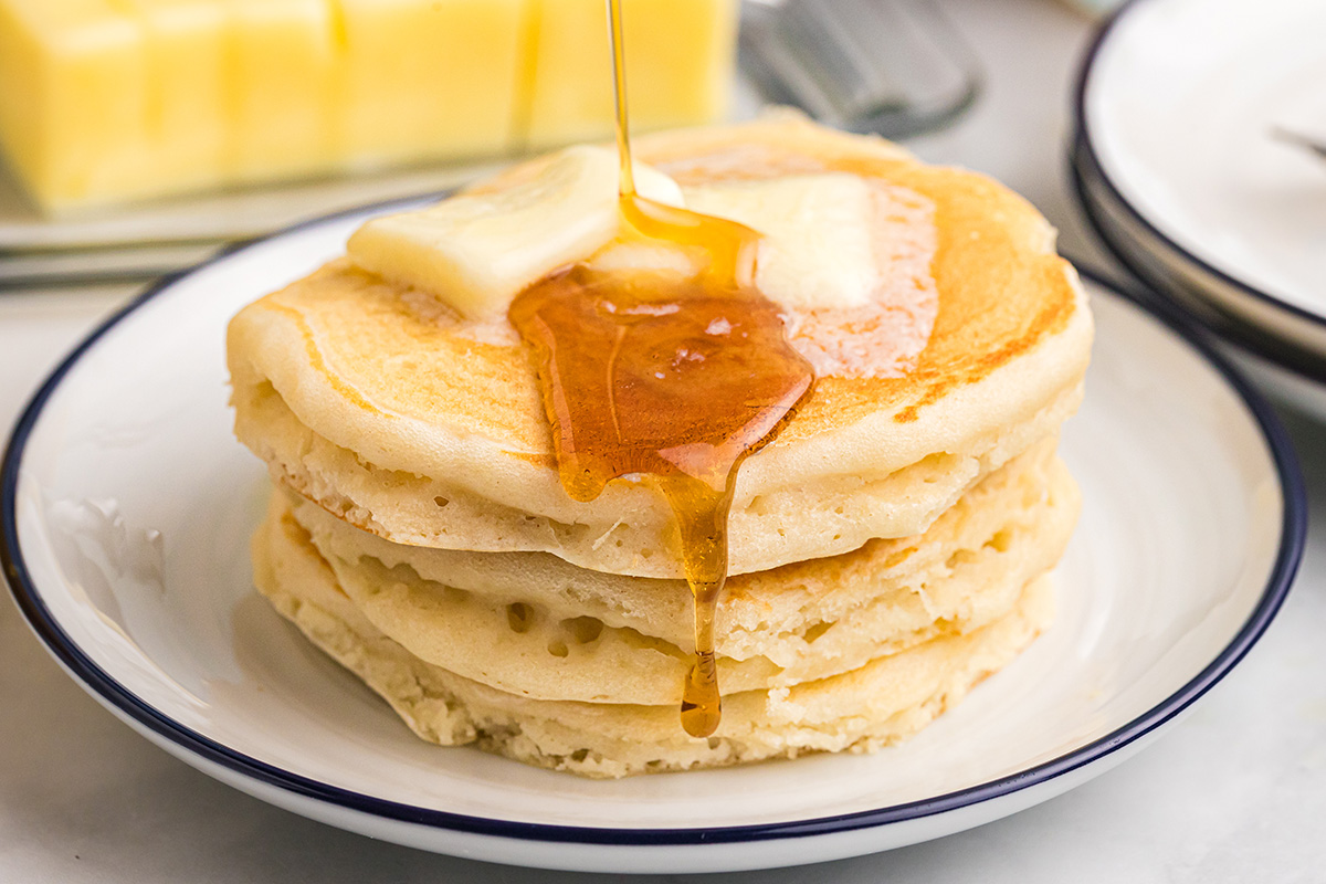 close up of syrup poured onto stack of buttermilk pancakes
