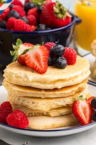 stack of pancakes on plate topped with fruit