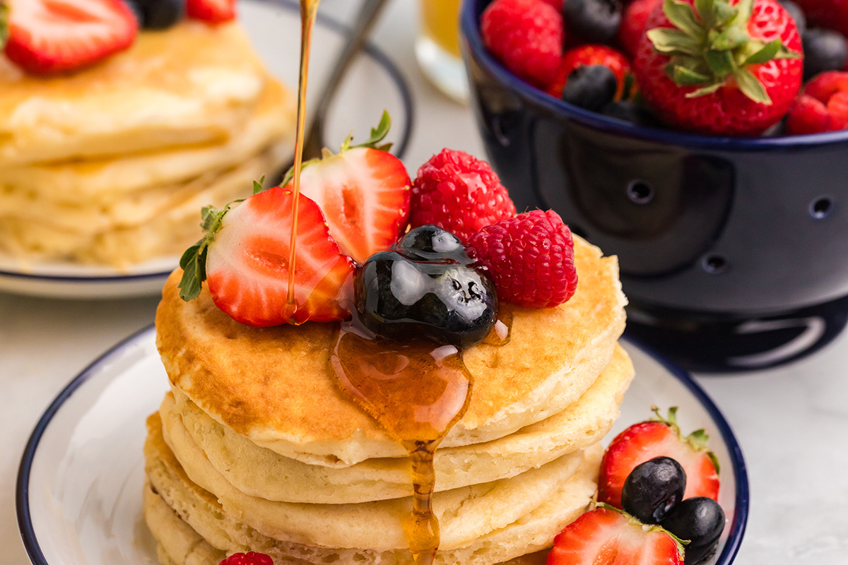 angled shot of syrup poured onto stack of pancakes