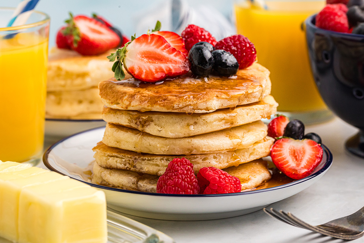 straight on shot of stack of buttermilk pancakes topped with fruit and syrup