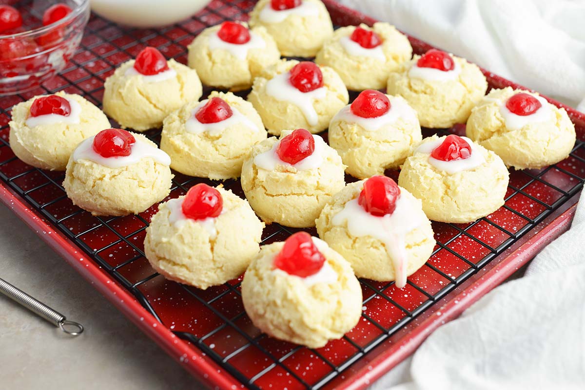 cheesecake cookies with powdered sugar icing with cherries on a wire cooling rack