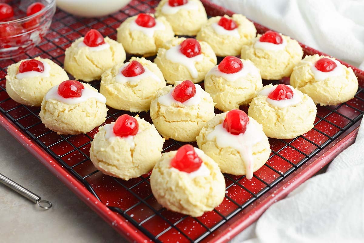 cheesecake cookies with powdered sugar icing with cherries on a wire cooling rack