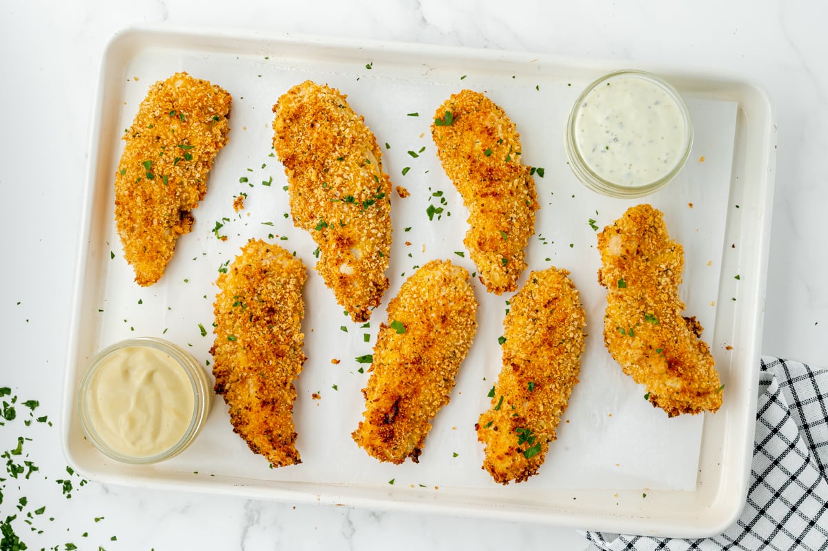 overhead shot of crispy oven baked chicken tenders on sheet pan with sauces