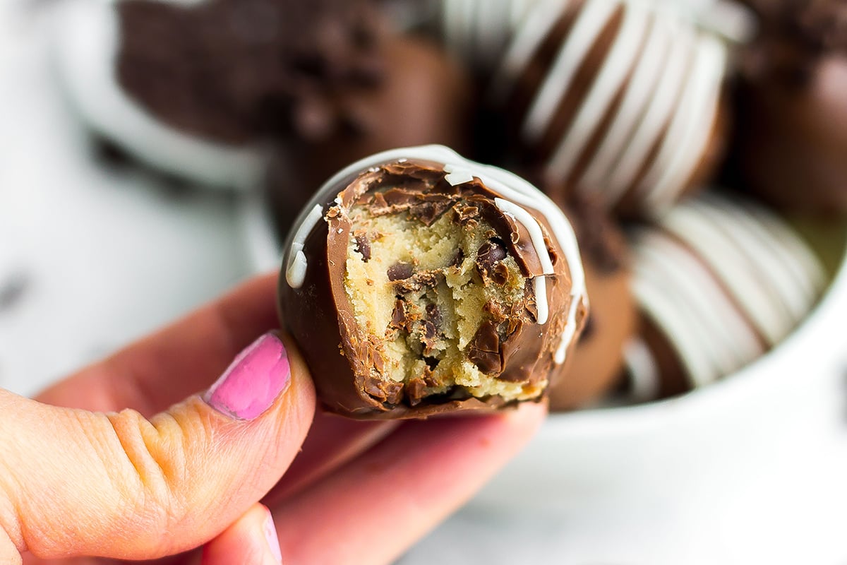 hand holding a cookie dough truffle with a bite taken out