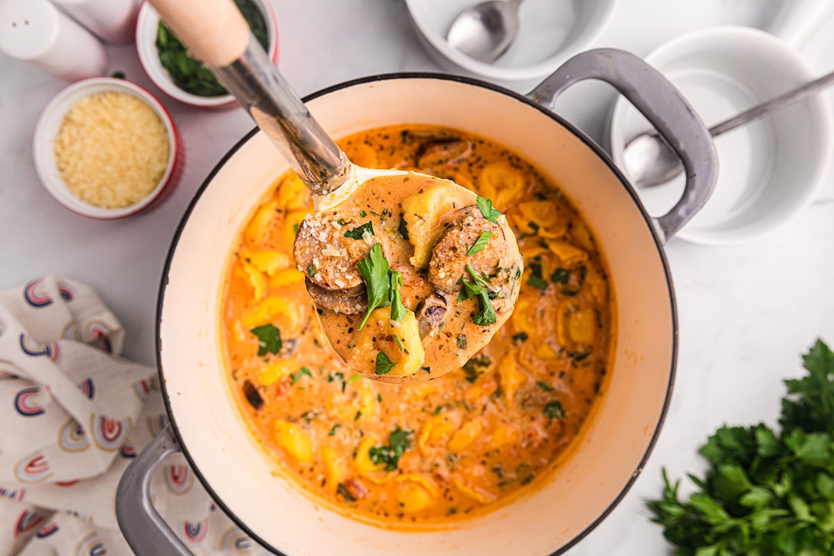 close up overhead shot of ladle full of creamy tortellini soup