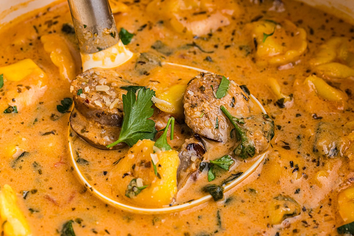 angled shot of ladle in pot of tortellini and sausage soup