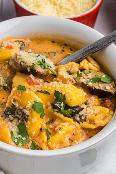 close up angled shot of spoon in bowl of tortellini and sausage soup