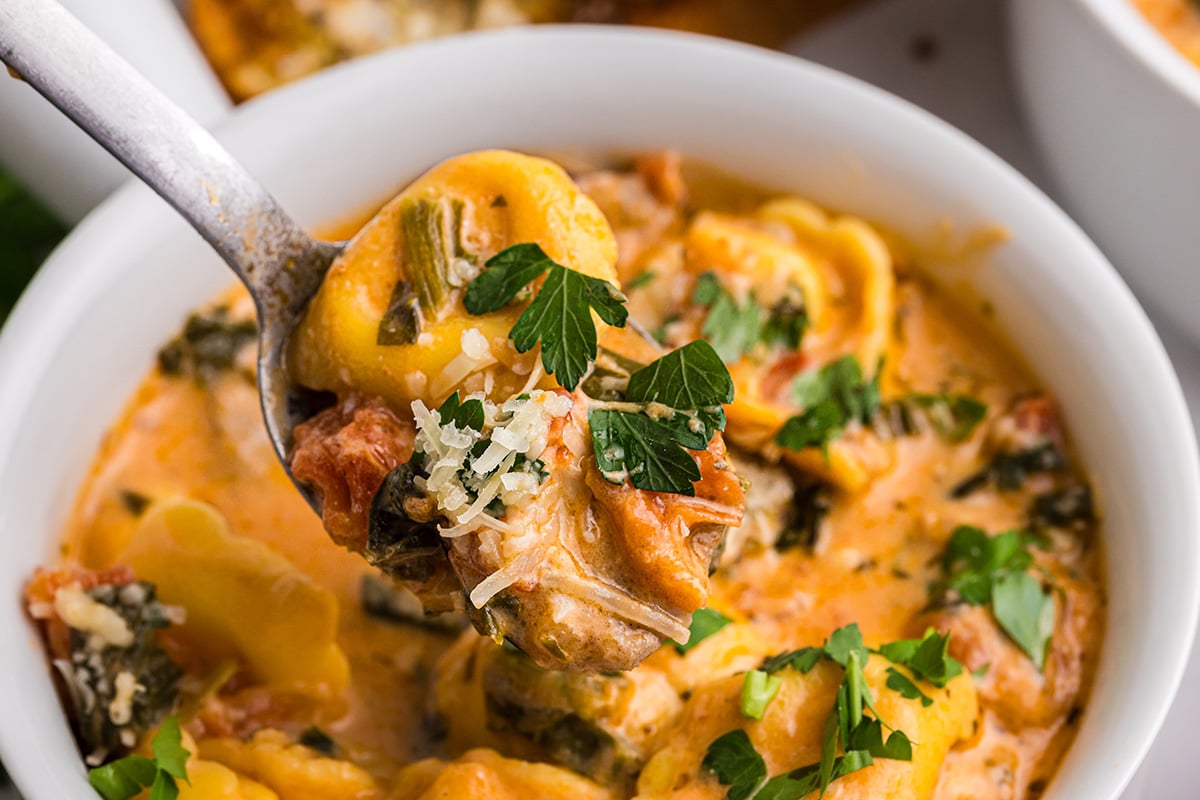 close up angled shot of bite of tortellini and sausage soup on spoon