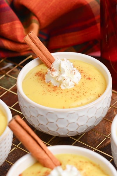 angled shot of bowls of eggnog pudding with whipped cream and cinnamon sticks on wire rack