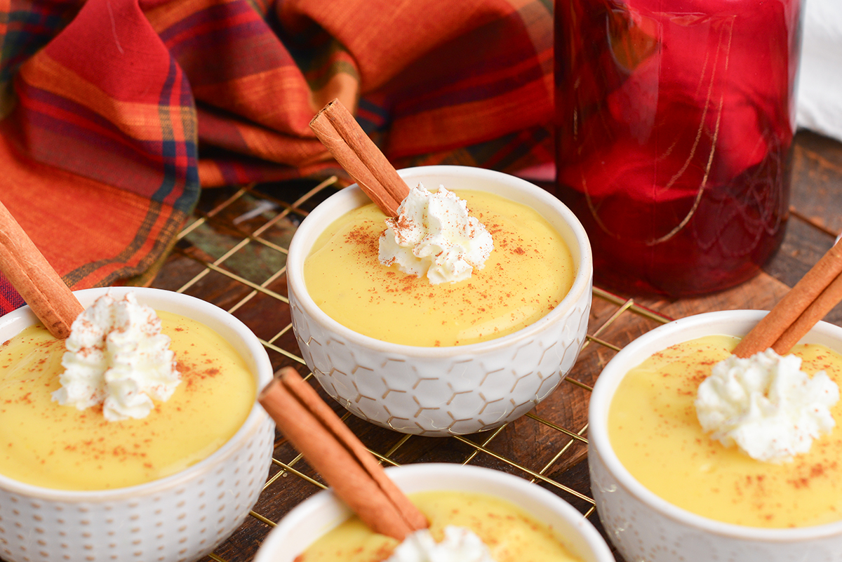 angled shot of bowls of eggnog pudding with whipped cream and cinnamon sticks on wire rack