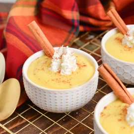 angled shot of bowls of eggnog pudding with whipped cream and cinnamon sticks