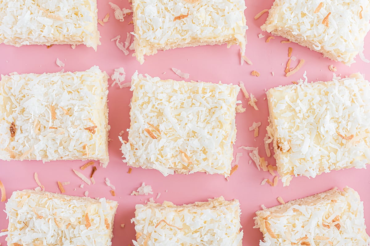 nine coconut bar squares sitting on a pink background