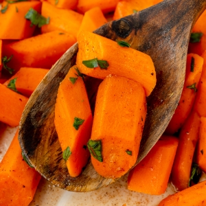 close up shot of honey glazed carrots on wooden spoon