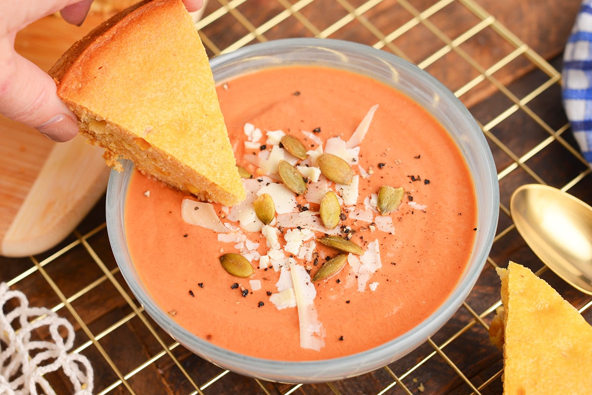 slice of cornbread dipping into bowl of soup