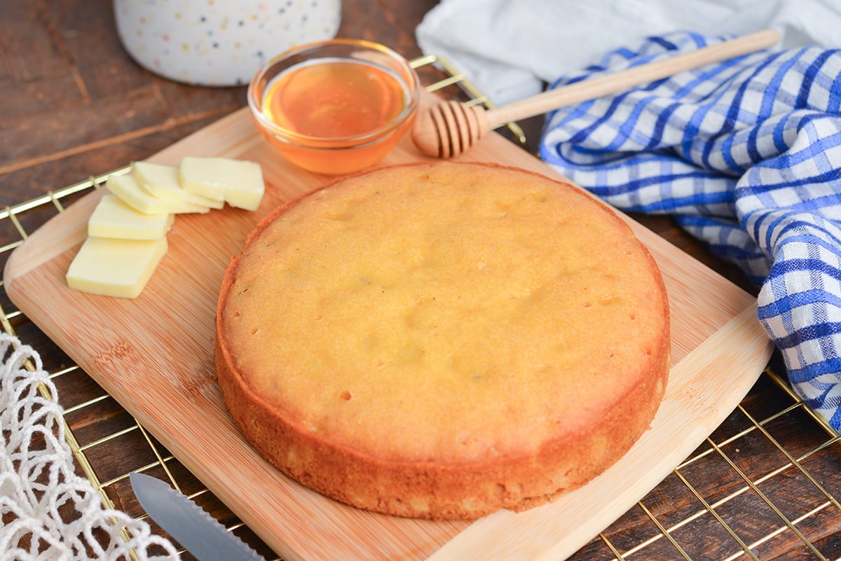 angled shot of instant pot cornbread on cutting board with butter and honey