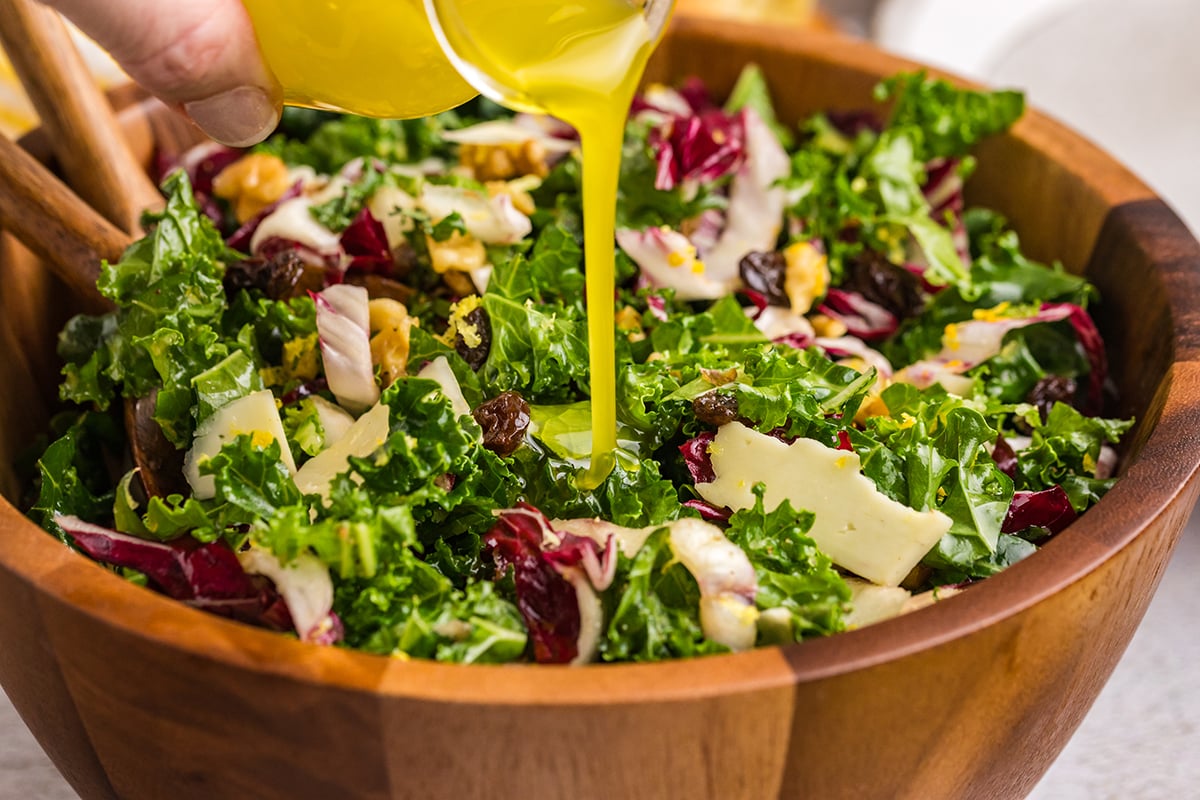 close up shot of lemon dressing poured into bowl of kale salad