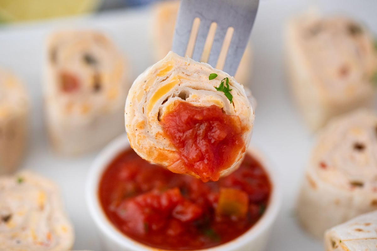 close up of fork dipping mexican pinwheels into salsa