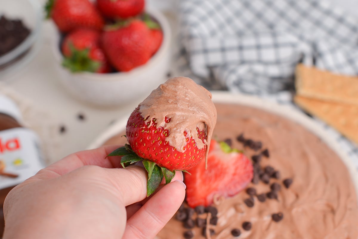 hand holding strawberry dipped into chocolate dip