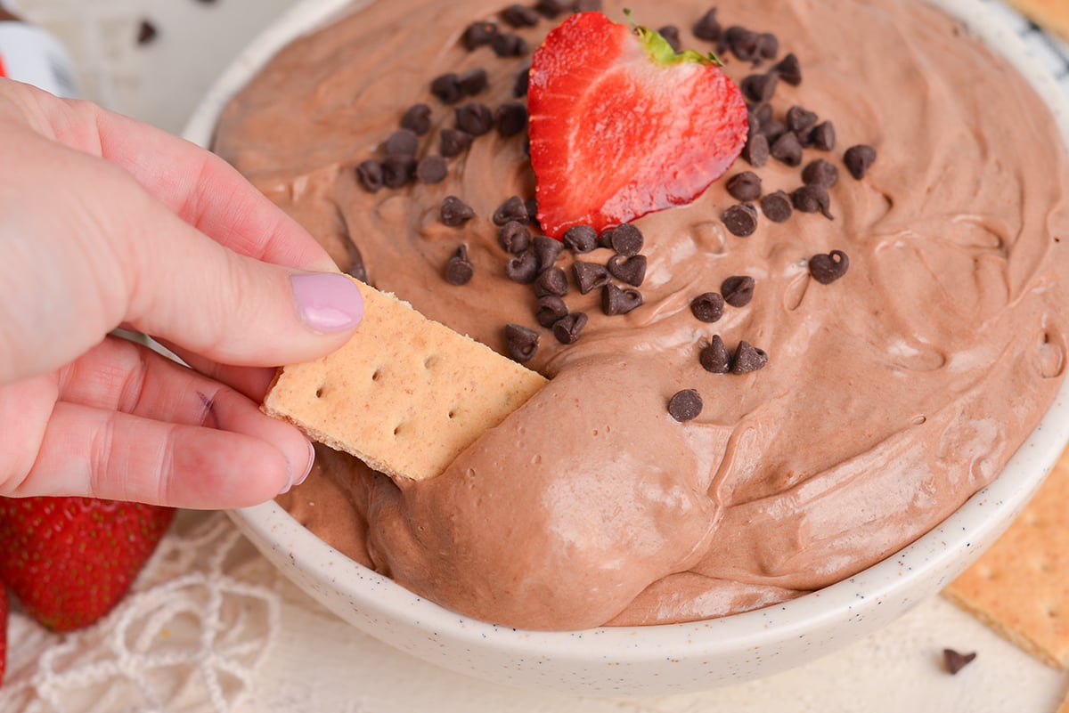 hand dipping graham cracker into nutella dip