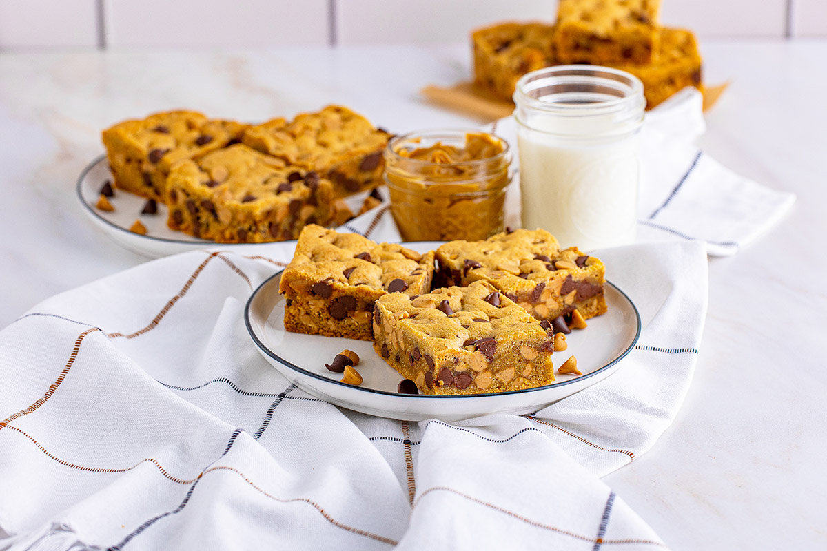 plates of peanut butter chocolate chip bars with milk and a glass jar of peanut butter