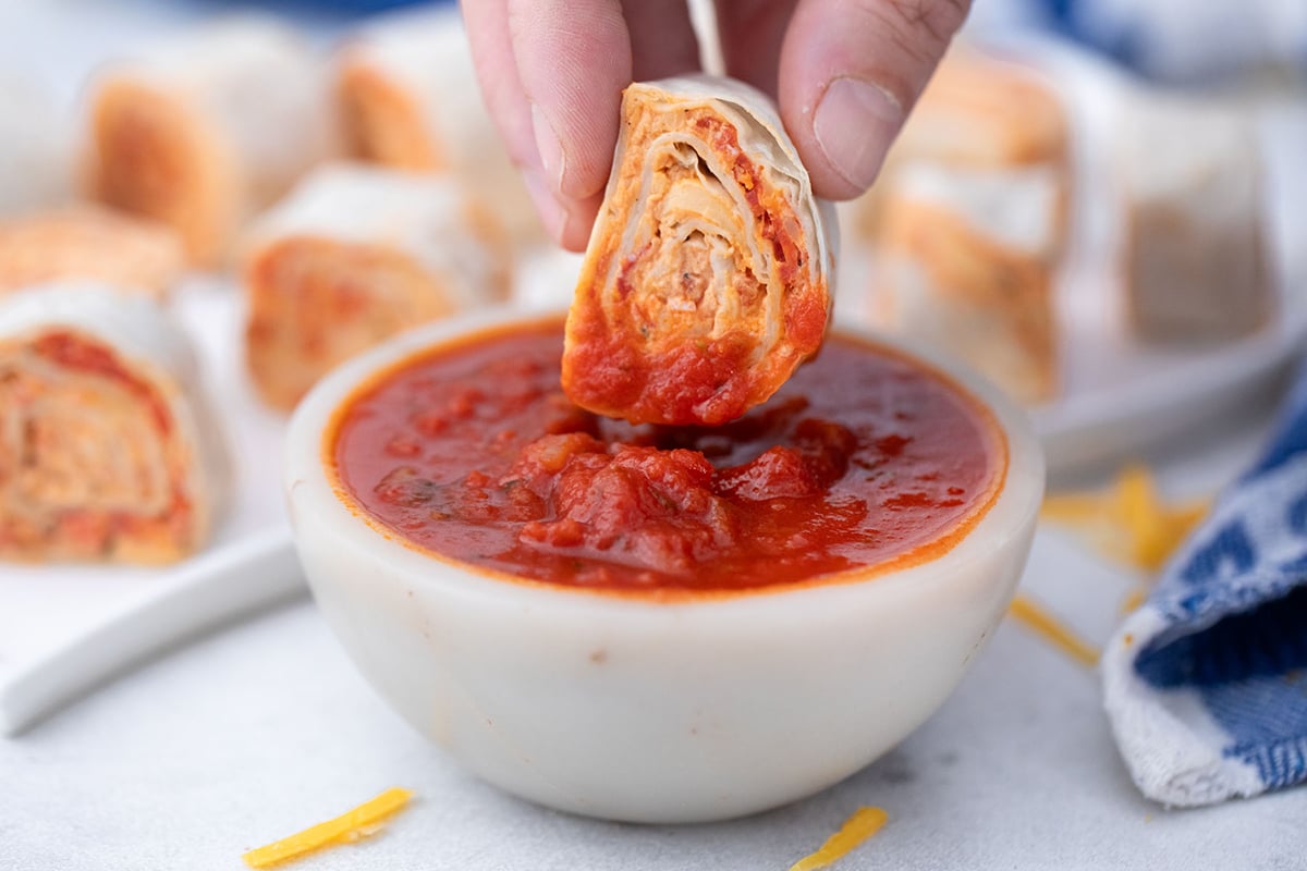 hand dipping pizza pinwheel into marinara sauce