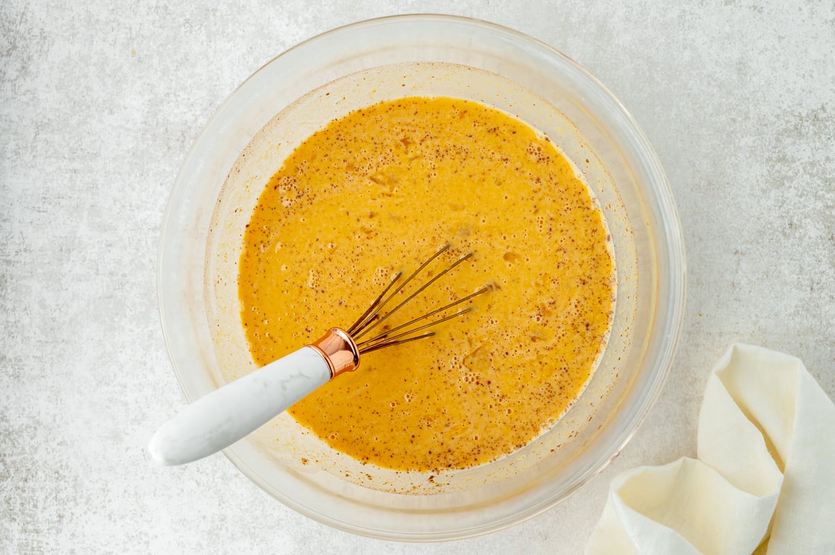 overhead shot of whisk in bowl of pumpkin custard