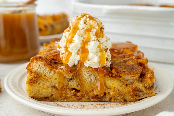 straight on shot of slice of pumpkin bread pudding topped with whipped cream and caramel