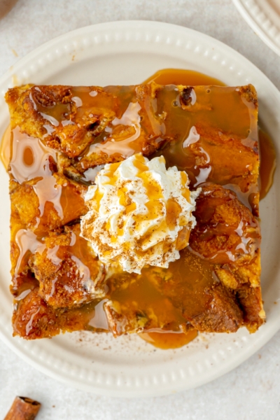 overhead shot of slice of pumpkin bread pudding topped with whipped cream and caramel