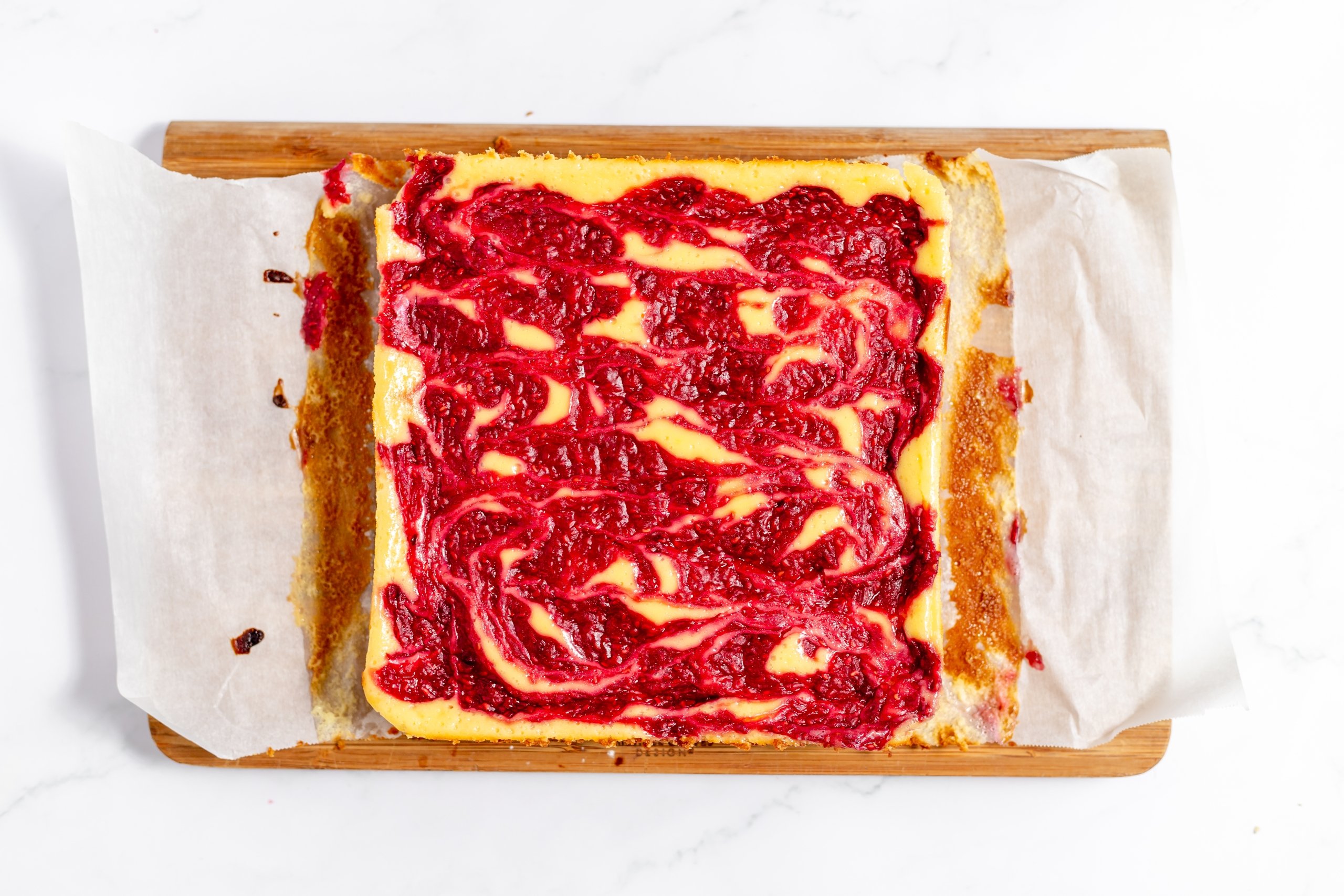 overhead of raspberry cheesecake bars on a parchment paper on a cutting board