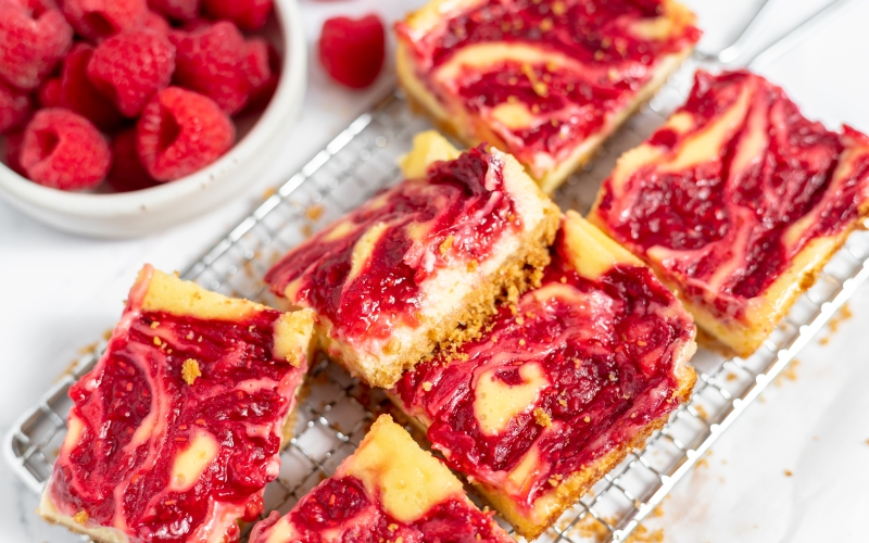 angle view of raspberry cheesecake bars on a wire rack